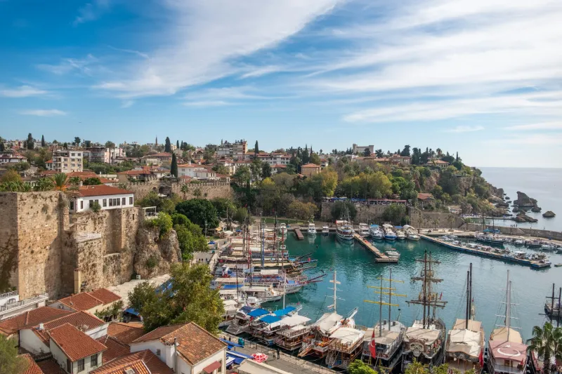 The old harbor of Kaleiçi in Antalya with wooden boats, the city walls and red-roofed houses above the bay