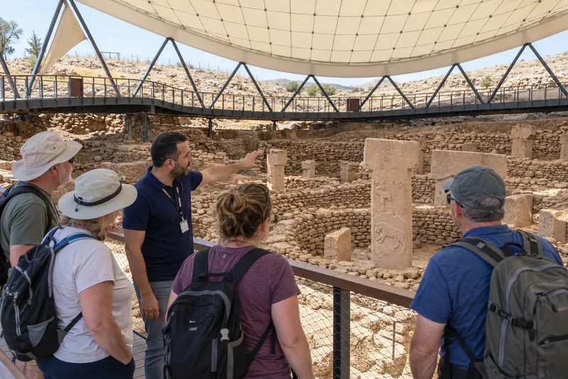 A licensed guide pointing out carved animal reliefs on a T-shaped pillar at Gobekli Tepe