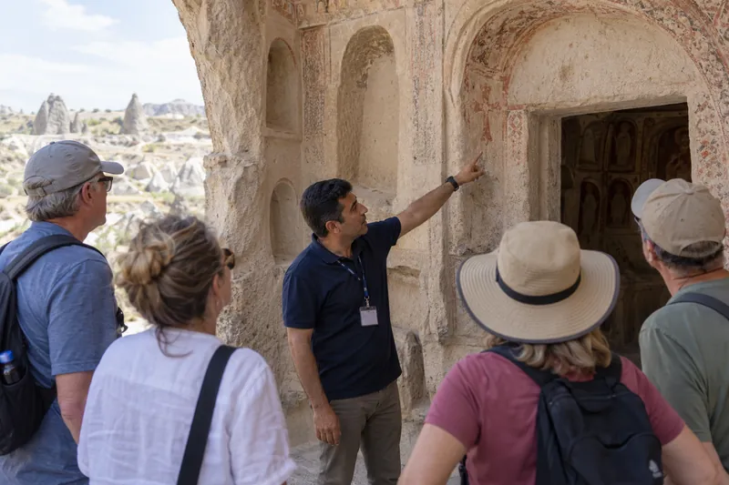 A licensed guide pointing out a painted cross at a rock-cut church in Goreme to a church group