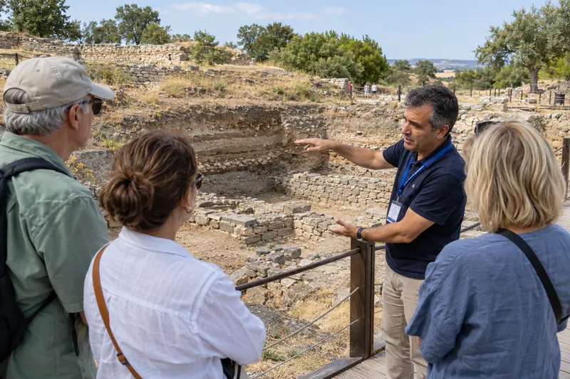 A licensed guide at Troy beside an excavation trench showing the layers of the ancient city